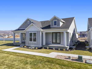 View of front facade with board and batten siding, roof with shingles, a porch, and a front lawn