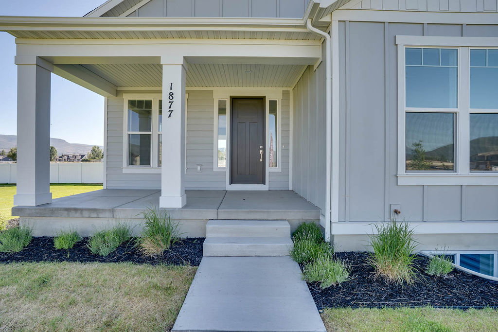 Welcoming concrete porch with two white square columns, light gray vertical siding, a dark entry door with a sidelight, and a white-framed window