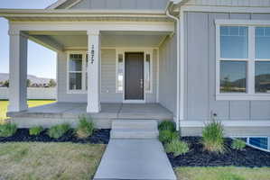 Welcoming concrete porch with two white square columns, light gray vertical siding, a dark entry door with a sidelight, and a white-framed window