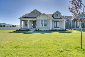 Light gray siding exterior with white trim, a covered front porch, an expansive green lawn, a white privacy fence, and a distant mountain backdrop
