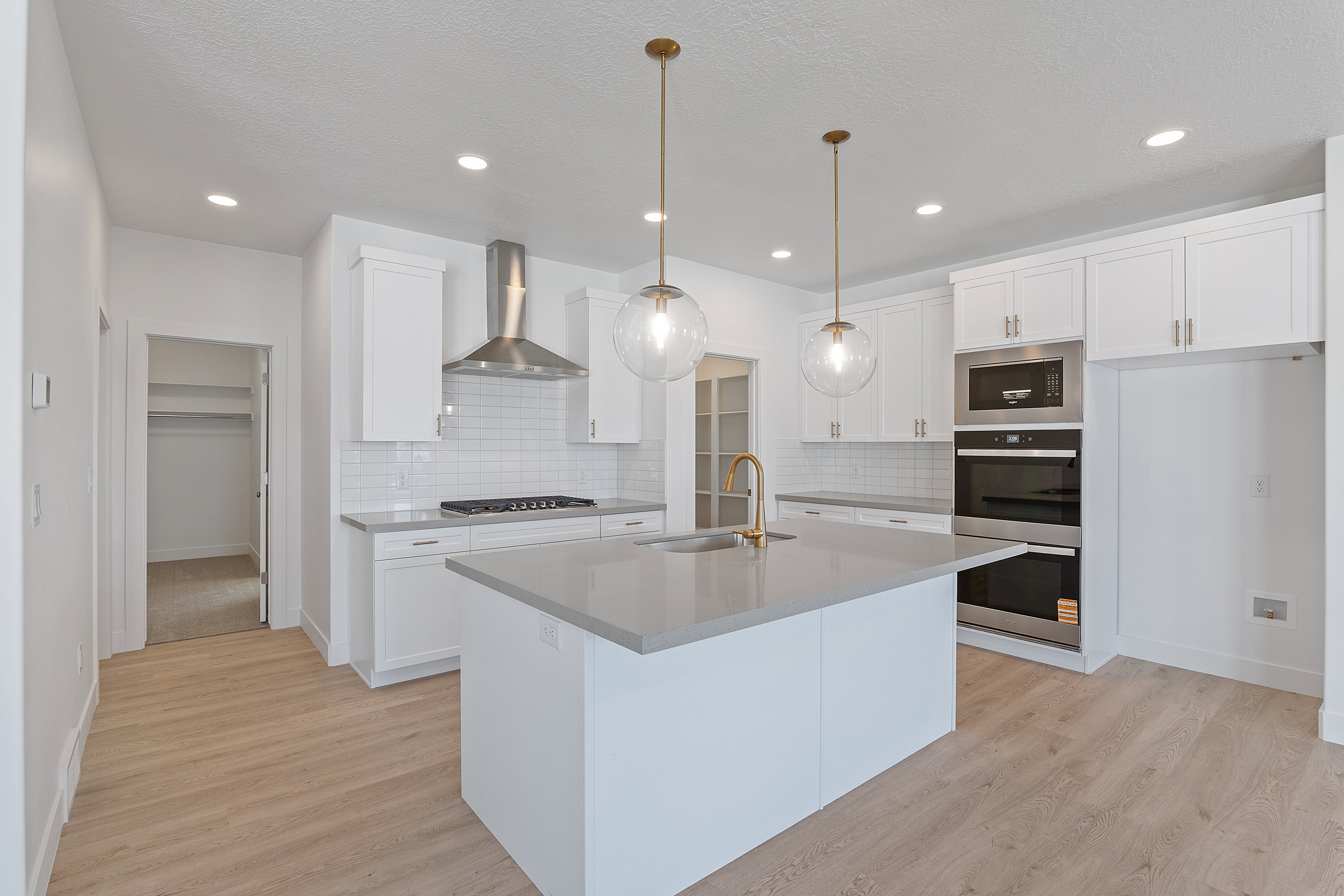Kitchen with white cabinetry, stainless steel appliances, an island with sink, wall chimney range hood, and recessed lighting