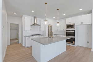 Kitchen with white cabinetry, stainless steel appliances, an island with sink, wall chimney range hood, and recessed lighting