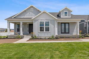 View of front facade with covered porch, board and batten siding, roof with shingles, and a front lawn
