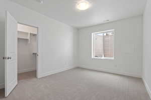Unfurnished bedroom with light carpet, a spacious closet, and a textured ceiling