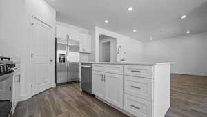 Kitchen with appliances with stainless steel finishes, white cabinetry, dark wood-type flooring, a center island with sink, and light countertops