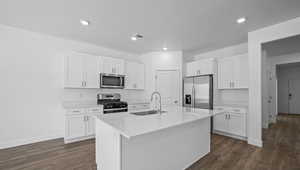 Kitchen with appliances with stainless steel finishes, white cabinetry, a kitchen island with sink, light countertops, and dark wood finished floors