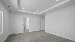 Unfurnished bedroom featuring carpet, recessed lighting, a tray ceiling, and connected bathroom
