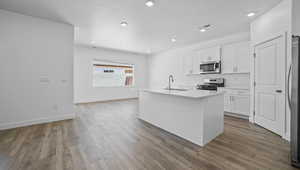 Kitchen featuring appliances with stainless steel finishes, white cabinetry, wood finished floors, a kitchen island with sink, and recessed lighting