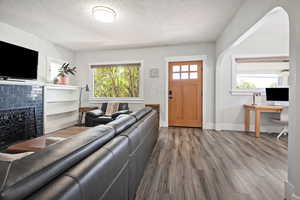 Living area with wood finished floors, a desk, a tile fireplace, and a textured ceiling