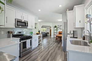 Kitchen with decorative backsplash, stainless steel appliances, arched walkways, wood finished floors, and white cabinets