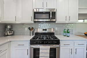 Kitchen featuring stainless steel appliances, white cabinets, and tasteful backsplash