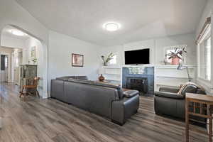 Living area featuring dark wood-style floors, arched walkways, a textured ceiling, and a tile fireplace