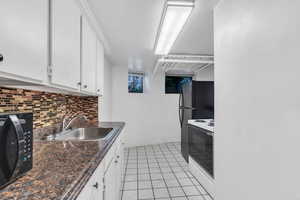 Kitchen featuring white electric range, white cabinets, dark countertops, light tile patterned floors, and decorative backsplash