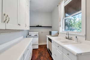 Kitchen with white appliances, white cabinetry, dark wood-style flooring, and light countertops
