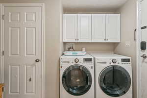 Laundry area featuring washing machine and clothes dryer, cabinet space, and a textured ceiling