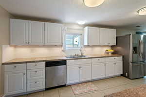 Kitchen with stainless steel appliances, white cabinets, a textured ceiling, and light tile patterned flooring