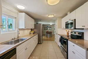 Kitchen with appliances with stainless steel finishes, white cabinets, light tile patterned floors, a textured ceiling, and decorative backsplash