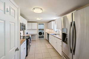 Kitchen featuring appliances with stainless steel finishes, washer and clothes dryer, a textured ceiling, white cabinets, and light countertops