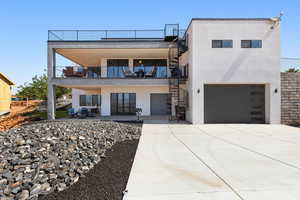 Back of property with a garage, stucco siding, stairs, concrete driveway, and a balcony