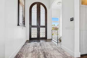 Foyer with french doors, a towering ceiling, arched walkways, and wood finished floors