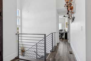 Corridor with dark wood finished floors, an office area, a towering ceiling, and an upstairs landing