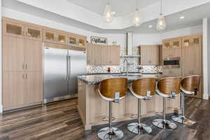 Kitchen with built in appliances, a kitchen island with sink, a breakfast bar area, light brown cabinetry, and decorative backsplash