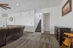 Carpeted living area with stairway, a textured ceiling, and ceiling fan