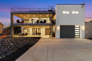 Back of property at dusk with stucco siding, stairway, an attached garage, concrete driveway, and a balcony