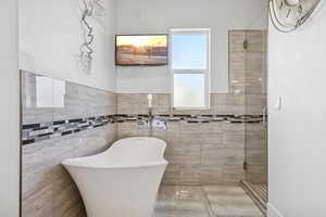 Bathroom featuring a freestanding tub, a stall shower, and tile walls