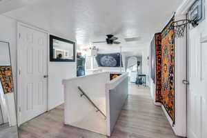 Hallway with an upstairs landing, a textured ceiling, and light wood-style flooring