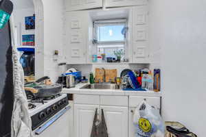 Kitchen with tile countertops, tasteful backsplash, white cabinetry, and white gas stove