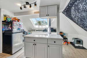 Kitchen with freestanding refrigerator, white cabinetry, a skylight, light wood finished floors, and a textured ceiling