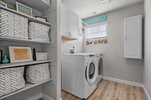 Laundry room featuring washer and clothes dryer, cabinet space, light wood-style floors, and a textured ceiling