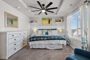 Carpeted bedroom featuring a raised ceiling and a ceiling fan