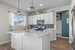 Kitchen with appliances with stainless steel finishes, backsplash, wood finished floors, white cabinetry, and light countertops