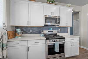 Kitchen with stainless steel appliances, decorative backsplash, white cabinetry, light countertops, and wood finished floors
