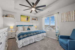 Carpeted bedroom featuring a raised ceiling and a ceiling fan