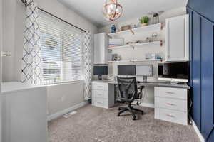 Carpeted office space featuring baseboards and a chandelier