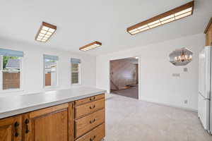 Kitchen with freestanding refrigerator, brown cabinetry, a chandelier, and light countertops