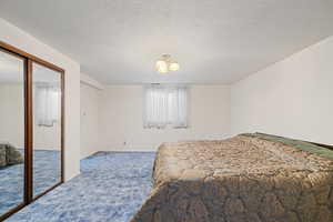 Carpeted bedroom featuring a textured ceiling and a closet