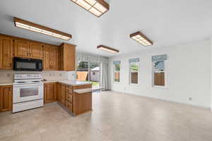 Kitchen featuring a peninsula, white range with electric stovetop, light countertops, black microwave, and brown cabinetry