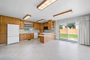 Kitchen with white appliances, light countertops, a peninsula, glass insert cabinets, and brown cabinetry