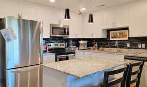 Kitchen featuring appliances with stainless steel finishes, a kitchen bar, white cabinetry, recessed lighting, and hanging light fixtures