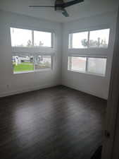 Empty room featuring plenty of natural light, dark wood-style floors, and a ceiling fan