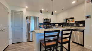 Kitchen featuring appliances with stainless steel finishes, backsplash, white cabinets, a kitchen island, and light wood-style flooring