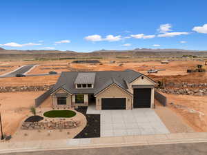 View of front of property featuring a garage, concrete driveway, stone siding, a mountain view, and view of desert