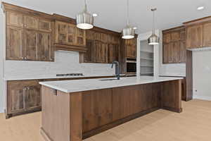 Kitchen featuring backsplash, light wood-style flooring, pendant lighting, light stone counters, and a large island with sink