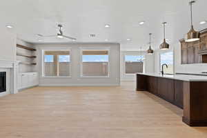 Kitchen featuring light countertops, a glass covered fireplace, light wood-type flooring, a kitchen island with sink, and a ceiling fan