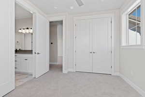 Unfurnished bedroom with light colored carpet, a closet, ensuite bathroom, and ceiling fan