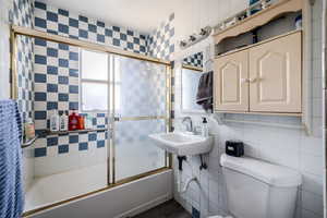 Bathroom featuring tile walls, shower / bath combination with glass door, and tasteful backsplash